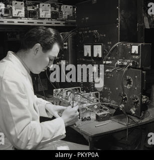 Années 1950, historique, un homme en blouse blanche du technicien test des composants internes d'un récepteur radio sans fil à Radio Bush, un des leaders de l'électronique grand public britannique en cette ère de l'entreprise. Banque D'Images