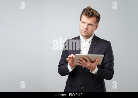 L'examen de nouveau gadget. Certains jeunes bel homme en chemise et cravate travaillant sur tablette numérique Banque D'Images