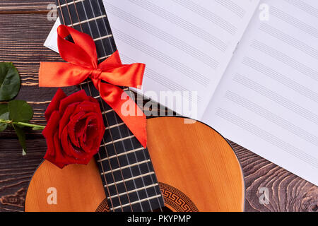 La guitare et les notes de musique sur fond de bois. Guitare rétro avec ruban rouge. Rose et feuilles de notes de musique. Fond musical romantique. Banque D'Images