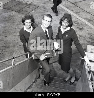 Années 1960, historique, représentant le vol avec la compagnie aérienne nationale, Air Finn debout sur les étapes d'embarquement à l'avion pour une photo avec deux des femmes de la compagnie aérienne, l'équipage de cabine exerçant son don d'une petite entreprise de bord sac de voyage, Londres, Angleterre, Royaume-Uni. Banque D'Images