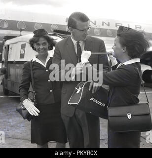 Années 1960, historique, un gentleman en vol avec la compagnie aérienne nationale, Finnair accordée un cadeau d'un petit sac de voyage à partir de l'entreprise un des femmes en uniforme, les membres de l'équipage de cabine, Londres, Angleterre, Royaume-Uni. Banque D'Images