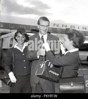 Années 1960, historique, un gentleman en vol avec la compagnie aérienne nationale, Finnair accordée un cadeau d'un petit sac de voyage desire de l'un de l'avion en uniforme de la femme de l'équipage de cabine, Londres, Angleterre, Royaume-Uni. Banque D'Images