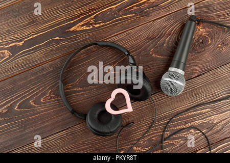 Casque et microphone sur fond de bois. Écouteurs, microphone et coeur rose. Musique de l'amour. Banque D'Images
