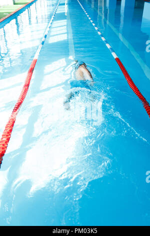 Photo de young man in blue cap natation sur le dos en piscine Banque D'Images