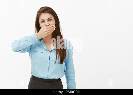 Femme a besoin de garder la bouche fermée. Portrait de femme européenne occasionnels brune en blouse bleue, couvrant la bouche avec de l'huile de palme et à regarder la caméra, gardant secret ou être offensé, ne parle pas de petit ami Banque D'Images