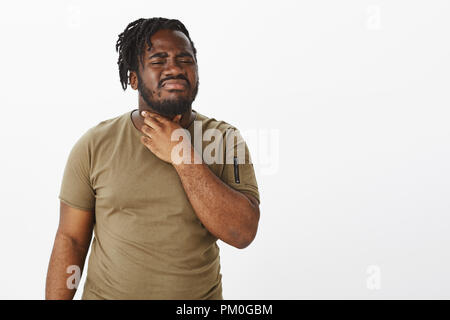 Guy partir se sentir malade après avoir mangé de la crème glacée. La peine à peau sombre malheureux homme grassouillet militaire en t-shirt, touchant le cou et froncer de sentiment douloureux, souffrant de maux de gorge ou d'allergie Banque D'Images