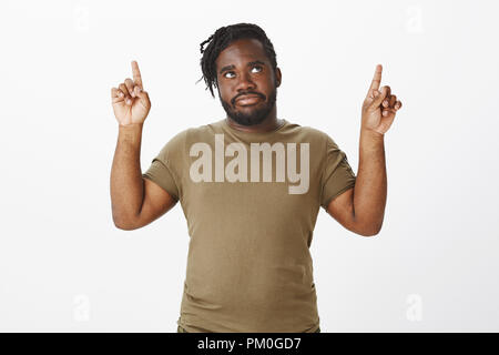 Portrait d'homme barbu africain peine déplut en tenue militaire, soulevant l'index, et à la pointe vers le haut avec l'expression ennuyé, être dérangé par le bruit des voisins Banque D'Images