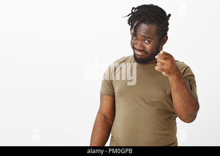 Vous êtes l'espoir. Portrait of handsome heureux l'homme à la peau sombre en tenue décontractée, faisant allusion à quelque chose en pointant sur appareil photo avec votre index, souriant curieusement sur mur gris Banque D'Images