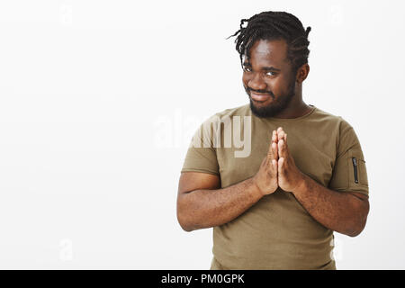 Guy de frotter les paumes, avoir de mauvaises plan diabolique. Intrigué funny africains-américains dans l'homme t-shirt olive, tenant les mains en prière, tilting head et souriant avec expression curieux, debout au-dessus de mur gris Banque D'Images