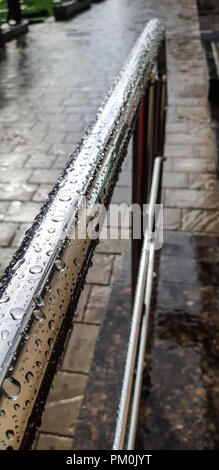 Main courante en métal chromé dans les gouttes de pluie sur un trottoir pavé. Banque D'Images