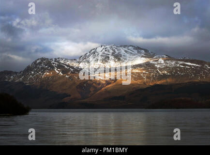 Une vue spectaculaire sur la neige, soleil en tête le sommet de Ben Lomond sous un lourd, gris et ciel orageux à Loch Lomond en Écosse. Banque D'Images