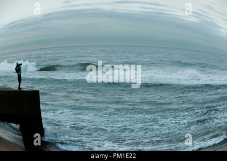 Durban, le KwaZulu-Natal, Afrique du Sud, seul adulte debout sur pier fisherman casting appât dans les vagues de l'Océan Indien, plage jour nuageux, le Bluff Banque D'Images