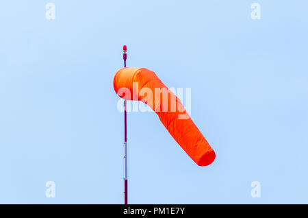 L'aérodrome d'orange un manche à vent sur un poteau blanc et rouge avec une balise rouge sur le dessus accroché dans une brise légère avec un bleu ciel sans nuages derrière Banque D'Images