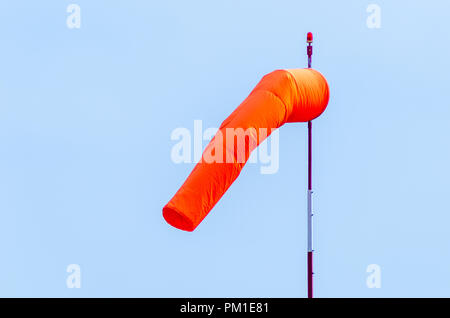 L'aérodrome d'orange un manche à vent sur un poteau blanc et rouge avec une balise rouge sur le dessus accroché dans une brise légère avec un bleu ciel sans nuages derrière Banque D'Images