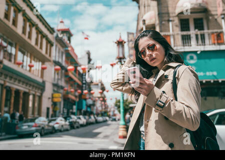 Jeune fille élégante et à la mode permanent en utilisant son téléphone portable en face de bâtiments Banque D'Images