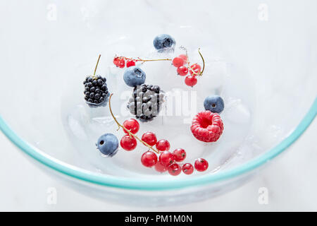 Close-up mûres, myrtilles, framboises, groseilles et des glaçons dans un bol transparent en verre sur une base en marbre gris . Vue d'en haut Banque D'Images