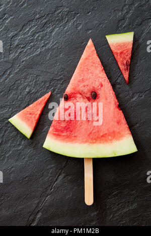 Une composition de morceaux de melon sucré sur un fond en béton noir. Un morceau de pastèque sous la forme d'une glace sur un bâton avec une copie de l'espace. Dessert sain. Mise à plat Banque D'Images