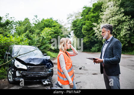 Un agent d'assurance à parler à une femme par la voiture sur la route après un accident. Banque D'Images