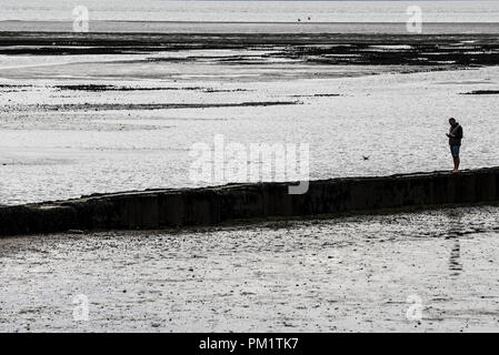 Homme seul figure debout sur un brise-lames de la mer dans l'estuaire de la Tamise. Marée basse. Silhouette. Seul. L Banque D'Images