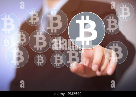 Bouton sur l'interface virtuelle Bitcoin afficher, homme d'affaires touchant le symbole monétaire Banque D'Images