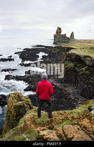 Falaises de basalte Londrangar. Tourist guy debout sur un rocher et regarde l'océan. Célèbre attraction touristique de l'Islande Banque D'Images