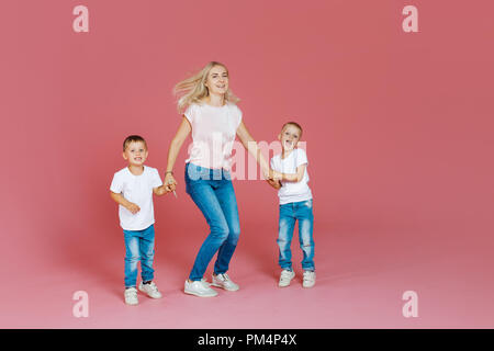 Belle blonde mère de deux fils heureux. Jeune femme et deux garçons de bébé, aller sur fond rose Banque D'Images