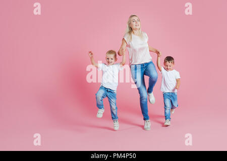 Belle blonde mère de deux fils heureux. Jeune femme et deux garçons de bébé, aller sur fond rose Banque D'Images