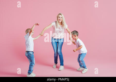 Belle blonde mère de deux fils heureux. Jeune femme et deux garçons de bébé, sauter et danser sur fond rose Banque D'Images