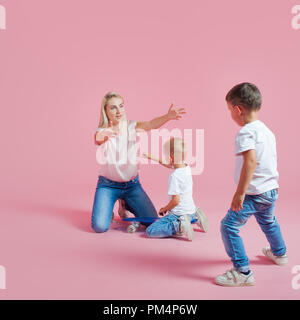 Belle blonde maman avec deux fils. Jeune femme et deux garçons de bébé, sur fond rose Banque D'Images