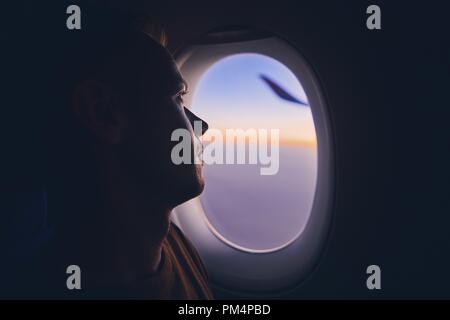 Silhouette de jeune homme voyageant par avion. Passager à la fenêtre pensif par en vol au lever du soleil. Banque D'Images