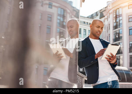 Loisirs de plein air. Jeune homme debout sur la ville rue leaning on wall browsing Internet sur tablette numérique concerné Banque D'Images