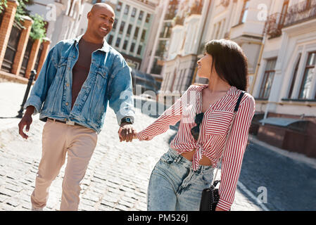 Diverses jeune couple walking on the city street holding hands regarder smiling smiling Banque D'Images