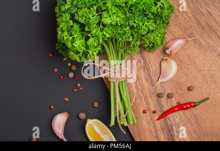 Un bouquet de persil frais bandé avec une corde avec un arc et un mélange d'épices et l'ail sur un tableau noir, vue du dessus Banque D'Images