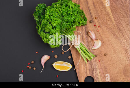 Un bouquet de persil frais bandé avec une corde avec un arc et un mélange d'épices et l'ail sur un tableau noir, vue du dessus Banque D'Images