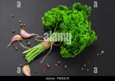 Un bouquet de persil frais bandé avec une corde avec un arc et un mélange d'épices et l'ail sur un tableau noir, vue du dessus Banque D'Images