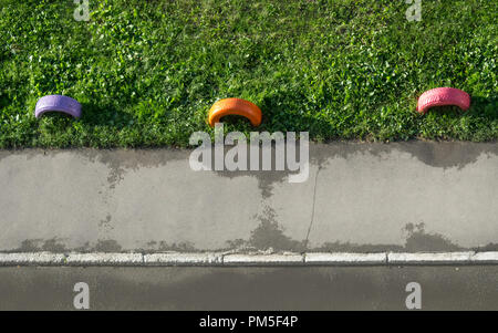 Vue de dessus colorés peints vieux pneus comme une clôture sur la pelouse de l'herbe verte le long du trottoir en asphalte avec bordure en pierre près de la route. Banque D'Images