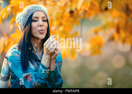 Portrait of young beautiful smiling positive young woman blowing dandelion in autumn park. Banque D'Images