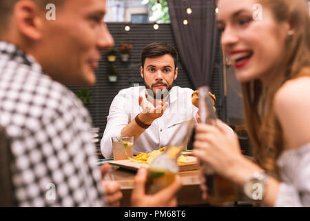 Jeune homme offensé en regardant ses amis tout en mangeant des hamburgers Banque D'Images