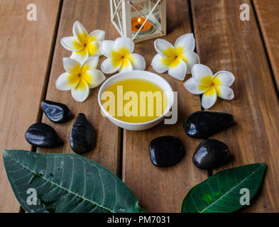 Huile de massage avec fleurs de plumeria et noir pierres rondes sur la surface en bois Banque D'Images