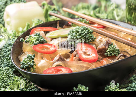 Nude asian plat épicé nouilles de verre épais couper les haricots mung fungosa en sauce aigre-douce Viande Légumes Poireaux poivrons dans un bol de baguettes sur le brocoli frais Banque D'Images