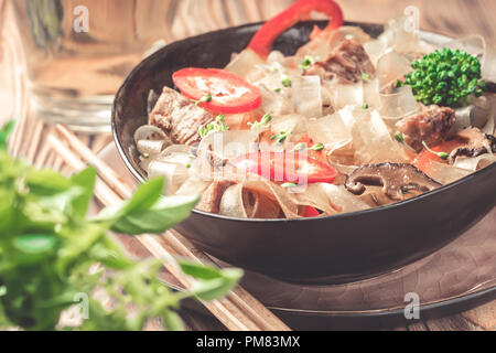 Nude asian plat épicé nouilles de verre épais couper les haricots mung fungosa en sauce aigre-douce viande légumes brocoli poivron poireau dans bol baguettes sur kitche Banque D'Images