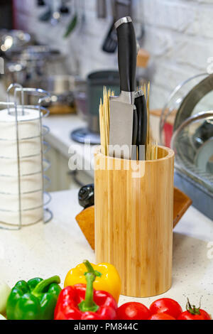 Des couteaux de cuisine dans un support en bois avec des pots d'épices et de légumes frais se situent sur une planche de bois. Close-up. Concept de cuisine Banque D'Images