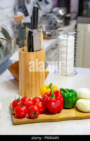 Des couteaux de cuisine dans un support en bois avec des pots d'épices et de légumes frais se situent sur une planche de bois. Close-up. Concept de cuisine Banque D'Images