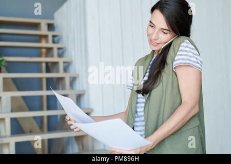 Portrait of young woman parlant par téléphone lors de la lecture de document Office, copy space Banque D'Images