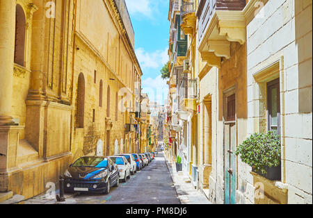 La promenade le long de l'immense mur de l'ancien bâtiment universitaire, également célèbre en tant que Campus de La Valette, face à St Paul Street, Valletta, Malte. Banque D'Images