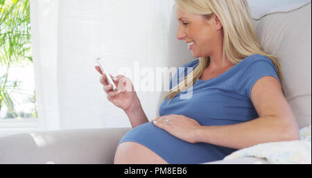 Beautiful pregnant woman texting on smartphone Banque D'Images