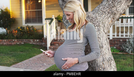 Happy pregnant woman texting on smartphone outdoors Banque D'Images