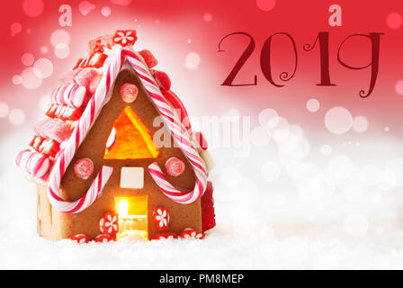 Gingerbread House dans un paysage enneigé comme décoration de Noël. Bougies pour une atmosphère romantique. Fond rouge avec effet de flou. 2019 Texte pour professionnels Banque D'Images