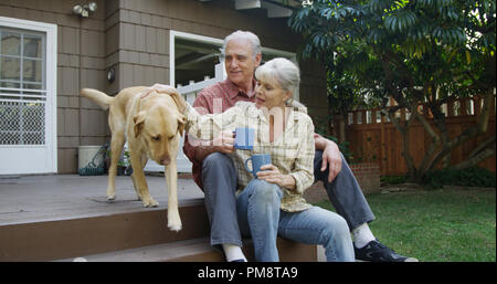 Senior couple having coffee petting dog dans leur cour Banque D'Images