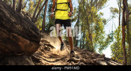 La section basse de trail runner s'exécutant sur des terrains rocheux. Les jambes du coureur masculin travaillant sur terrain extrême à l'extérieur. Banque D'Images